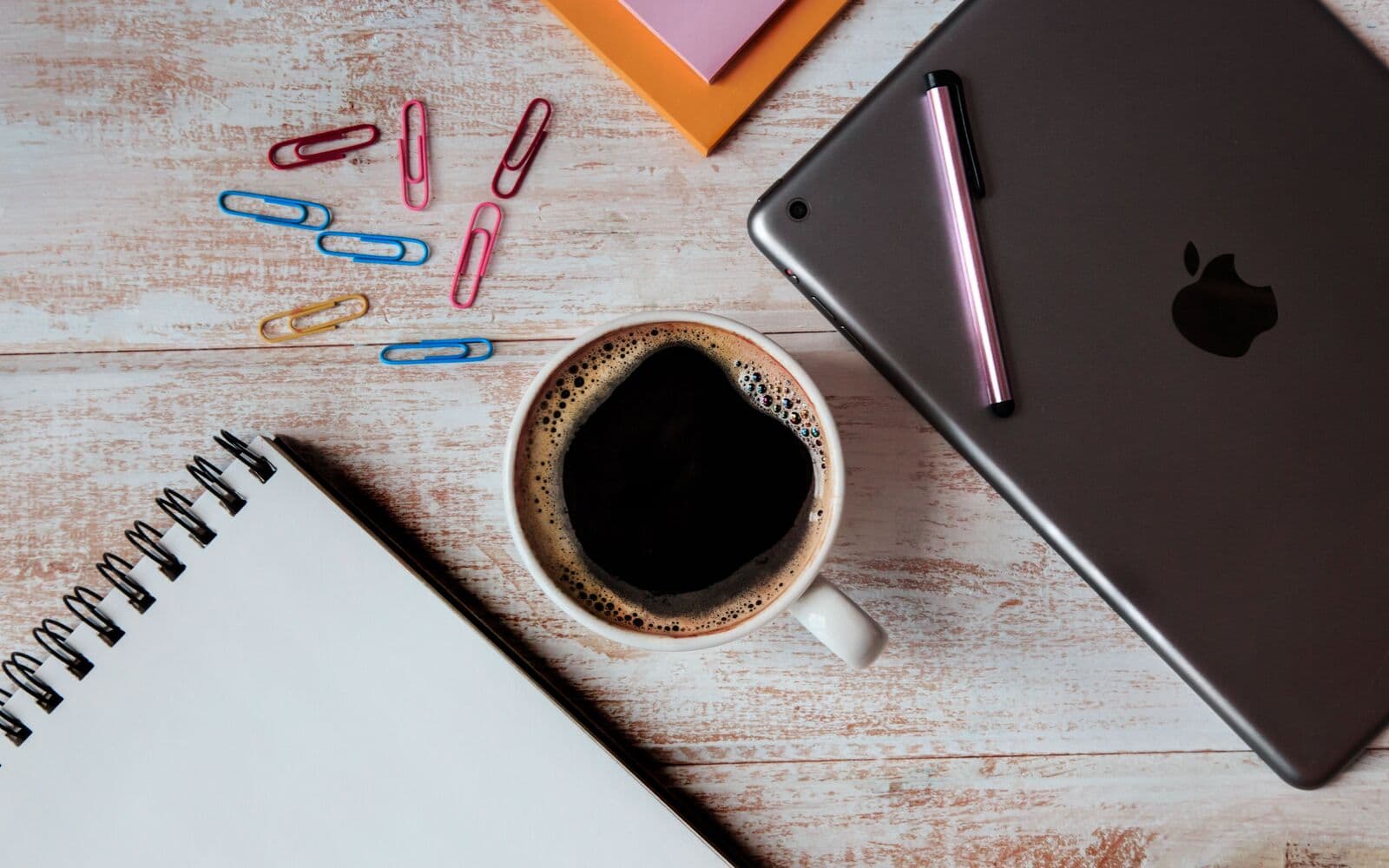 Coffee standing between MacBook and notebook.